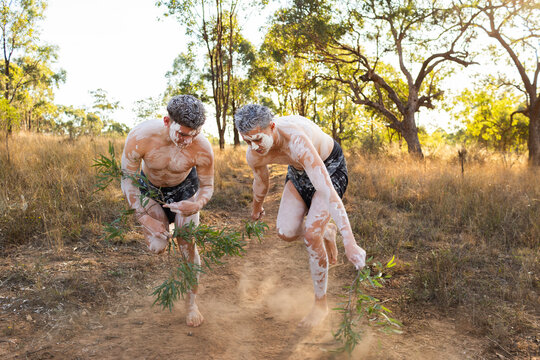 Young aboriginal men dancing with gum leaves and ochre body paint on country wearing lap laps
