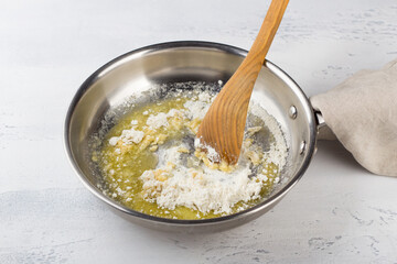 Mixing flour with melted butter in a frying pan on a light gray table. Making cheese pasta sauce, step by step, do it yourself, step 3