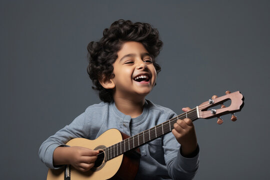 Happy indian kid playing guitar, a musical instrument