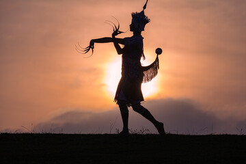 Nora performs dance moves in the field at sunset.beautiful sky background..The sun casts a silhouette on Nora..Nora is a form of traditional, folk performing arts in the southern region of Thailand..