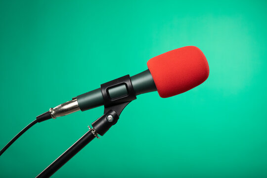 Microphone with red sponge on the microphone head standing isolated on green background.