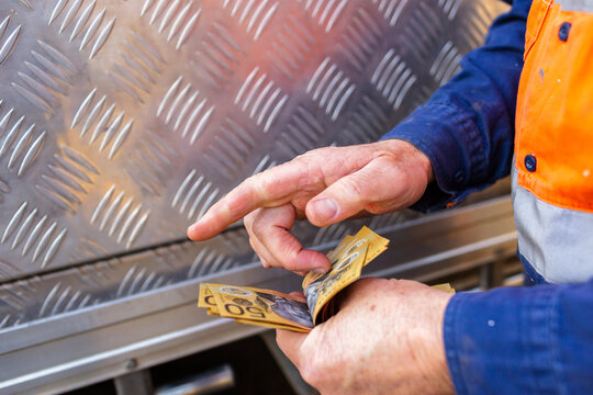 Hands of a handyman counting cash beside tradie ute