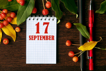 calendar date on wooden dark desktop background with autumn leaves and small apples.  September 17...