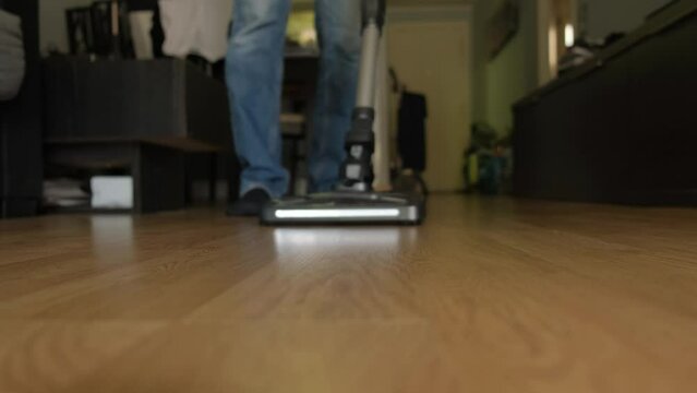 A cordless vacuum cleaner with a turbo brush and lighting cleans a laminate floor close-up.