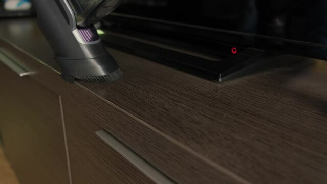 A cordless vacuum cleaner cleans dust on furniture close-up.