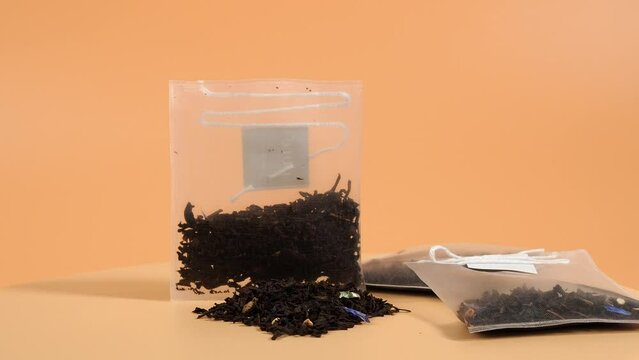 On an orange background, a transparent bag of black tea with the addition of the aroma of flowers rotates. Aromatic black tea bags. Close-up.