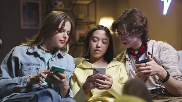 Group of multiethnic friends use smartphones. Group of friends use smartphones, communicate, laugh, cringe cause of online information in social networks on Internet. Friends spend good time together