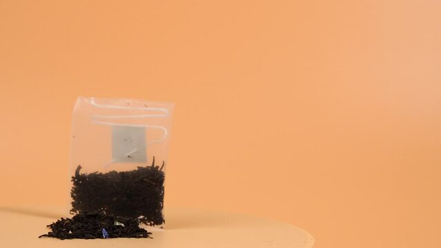 On an orange background, a transparent bag of black tea with the addition of the aroma of flowers rotates. Aromatic black tea bags. Close-up.