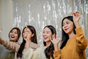 Cheerful friends enjoying home Birthday holiday party. Asian Friends hold lights with sparkling Sparkler celebrating Christmas or New Year eve party.