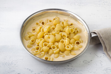 Cooking mac and cheese, American pasta. Adding cooked pasta to cheese sauce in a frying pan on a light gray background. Cooking stage