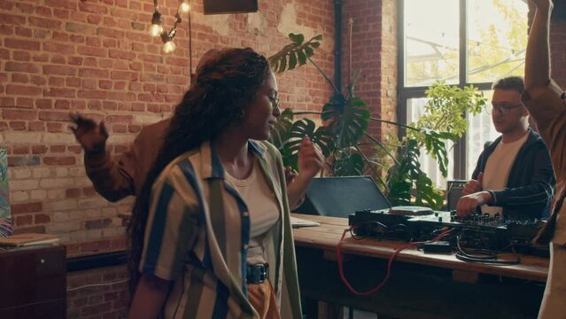 Slow motion shot of stylish young squatters dancing to music DJ playing with use of mixer in loft room