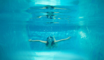 young woman swimming underwater in a personal pool with loose hair with glasses on head, summer leisure concept