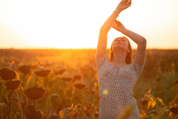young woman in evening sunlight in a sunflower field at summer sunset, girl holding hands in the...