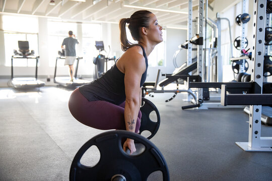 Strong, muscular woman lifting weights in gym during workout. Competitive female weightlifter
