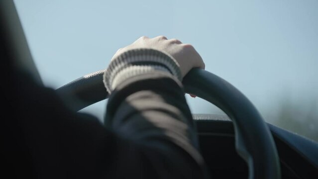 Slow motion close up view of young girl's hands on car and automobile steering wheel with window and dashboard in background as she travels on a sunny day towards her destination
