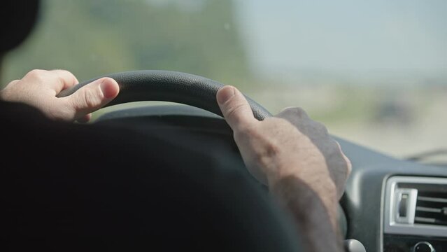 Slow motion of man's hands and arms on steering wheel driving a car on a road with window in background during a sunny summer day moving towards destination