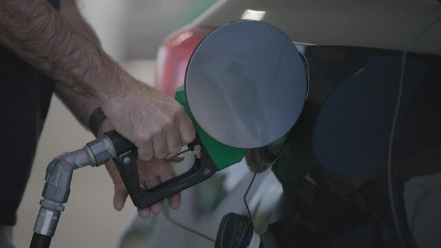 Slow motion of man and his hands filling his automobile car tank with unleaded gas and petroleum fuel at small gas station in close up on grey vehicle