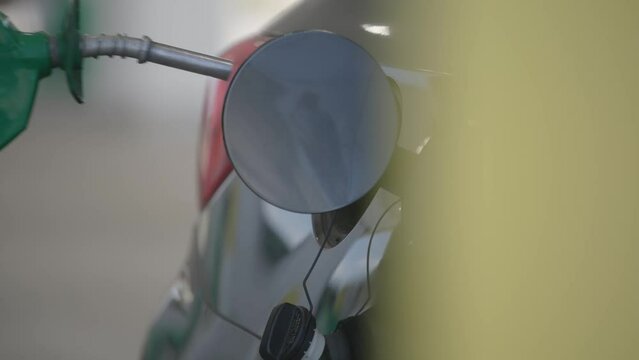 Slow motion of man and his hands filling his automobile car tank with unleaded gas and petroleum fuel at small gas station in close up on grey vehicle