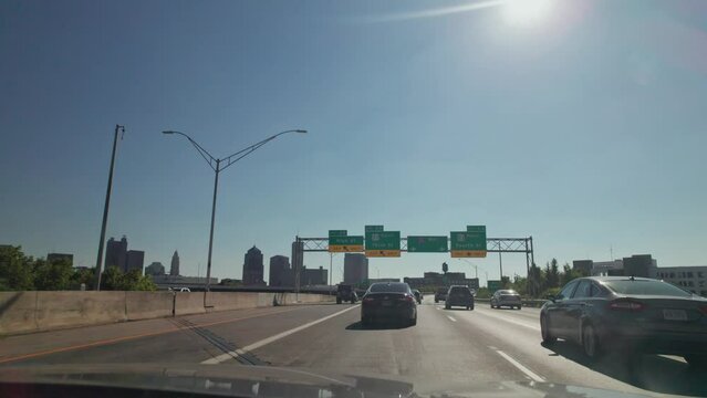 Car driver point of view pov moving towards downtown Columbus, Ohio in interstate 670 multi-lane highway while stuck in traffic and surrounded by cars during a sunny summer day