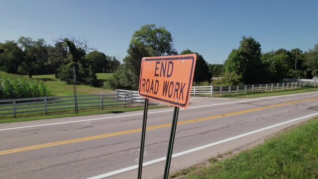 Rotating view of orange road sign label signaling with "End Road Work" text on side of street near construction site on rural roadside 