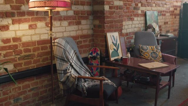 No people shot of old-fashioned armchairs, table, floor lamp in loft room with brick wall, 90s aesthetics
