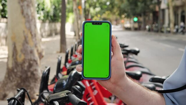 Phone chroma key with Tourist man take Electric Kick scooter or bike bicycle in sharing parking lot, green screen smartphone, tourist application. Sharing business in city, eco transportation
