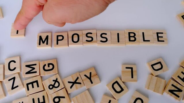 close-up female hand holds square wooden alphabet blocks, word impossible turns into word possible on white background, self-identification, concept self-motivation and happiness, creative meaning