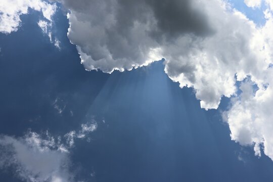 Sunbeams shining from behind a white cloud on a blue sky
