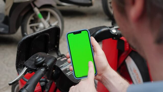 Phone chroma key with Tourist man take Electric Kick scooter or bike bicycle in sharing parking lot, green screen smartphone, tourist application. Sharing business in city, eco transportation