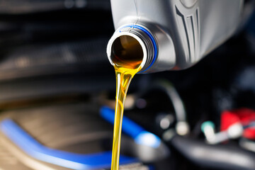 Pour car lubricant from a gray bottle on the background of the engine. Oil change service, auto repair shop Technology and transportation industry