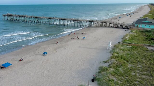 aerial footage of a gorgeous summer landscape at Kure Beach with people relaxing on the beach and fishing on Kure Pier, ocean water, waves and blue sky in Wilmington North Carolina USA