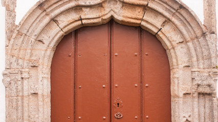 Fototapeta na wymiar Puerta de madera roja en arco de piedra de iglesia rural