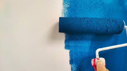 roller with blue paint on a white wall - Powered by Adobe