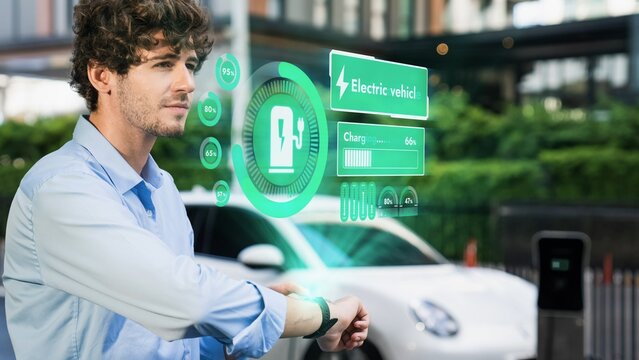 Businessman checking EV car battery status in hologram from smartwactch while recharging from charging station. Modern urban lifestyle and eco-friendly electric car utilization to reduce CO2. Peruse