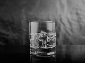 Whisky tumbler with ice and spirits in it, shot in black and white in moody scene.