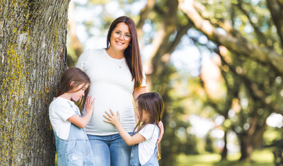 Pregnant woman posing in the parkwith her two childs
