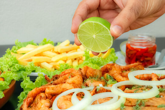 M&atilde;o espremendo lim&atilde;o em por&ccedil;&atilde;o de camar&atilde;o frito e por&ccedil;&atilde;o de batatas fritas