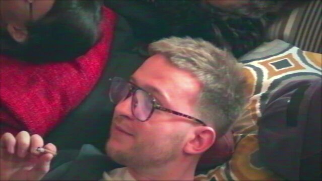 From above VHS shot of young Black and Caucasian squatters relaxing on mats on floor in abandoned house smoking and talking
