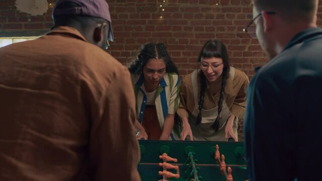 Ethnically diverse young men and women playing table soccer in loft room, women winning game