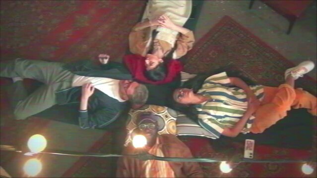 VHS shot of ethnically diverse young squatters relaxing together on mats on floor with old carpets on it