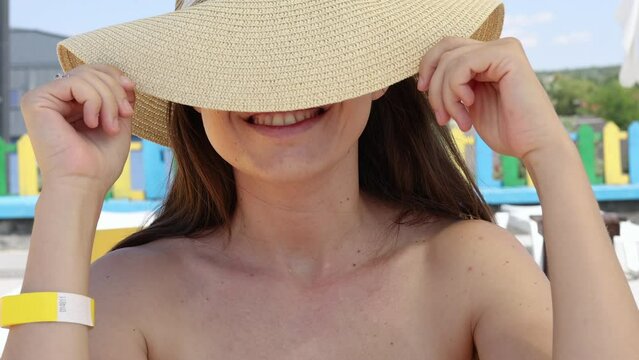 millennial woman on pool side or resting on lounger chair with beach hat on head or in front of breast. unperfect body fat on belly, after childbirth skin not elastic. summer vacation time smiling fem