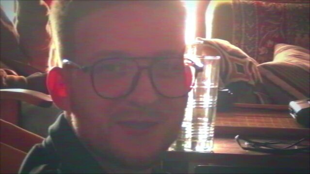 VHS zoom in portrait of cheerful young male squatter sitting on floor smiling at camera while watching movie with friends