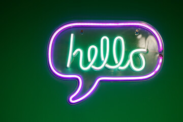 Green and purple neon lamp with word hello over the green wall