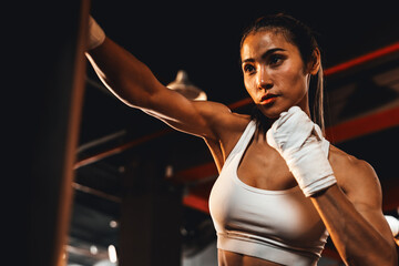 Asian female Muya Thai boxer training, wrapped hand punching at kicking bag at the gym. Healthy...