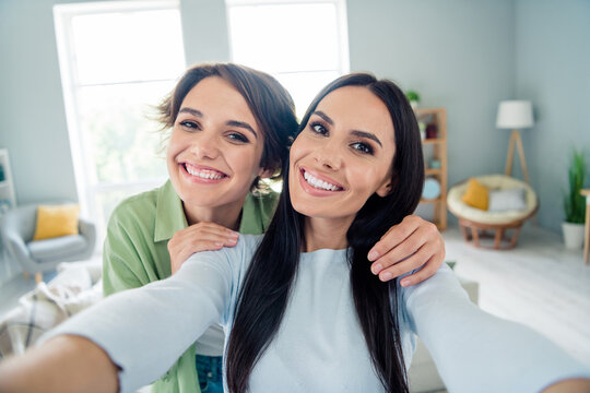 Photo of two pretty positive girls embrace beaming smile take selfie have good mood free time apartment indoors