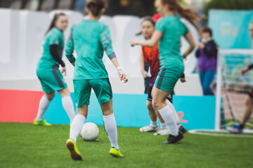 Female football street match outdoor game on an artificial astroturf lawn, girls play soccer game on a pitch field, young women participate in football competition on a stadium with green grass