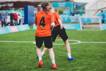Female football street match outdoor game on an artificial astroturf lawn, girls play soccer game on a pitch field, young women participate in football competition on a stadium with green grass