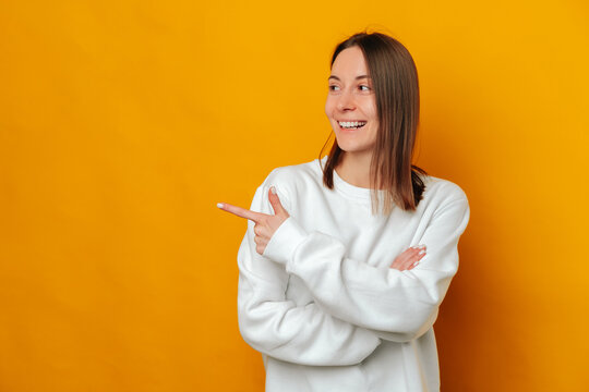 Cool studio portrait of a young woman pointing aside on yellow background.