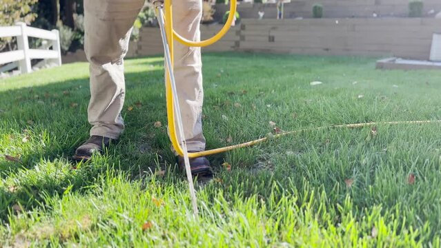 A low angle view of an exterminator injecting termite treatment in the backyard of a home.  	