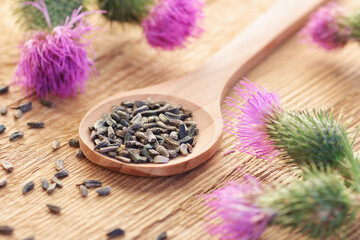 Thistle seeds in wooden spoon and flowers on rustic background, closeup, natural medicine, healthy...